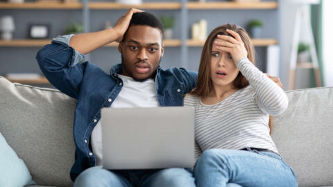 surprised couple on a couch reading their computer