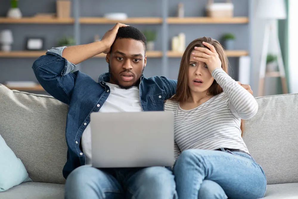 surprised couple on a couch reading their computer