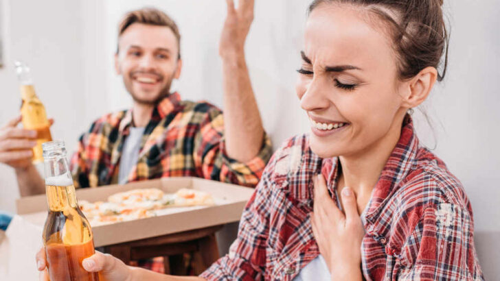 2 adults laughing while eating pizza