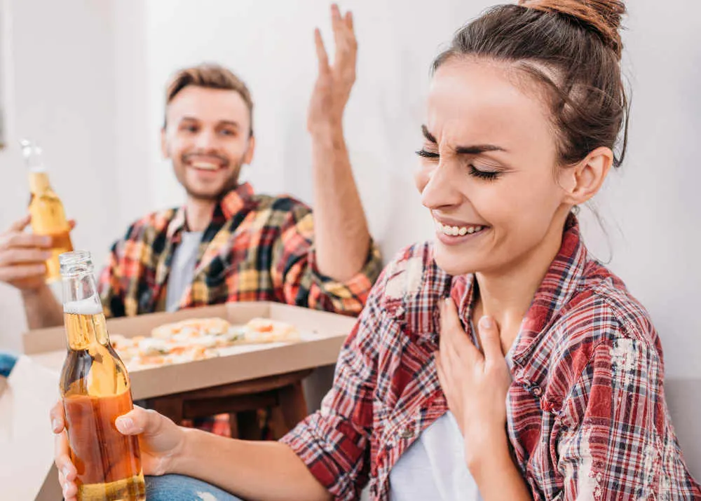 2 adults laughing while eating pizza