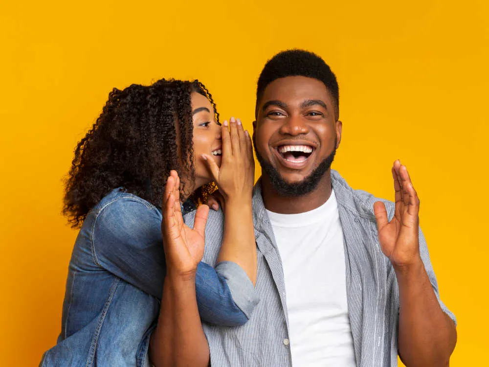 woman whispering a joke to a guy who is laughing