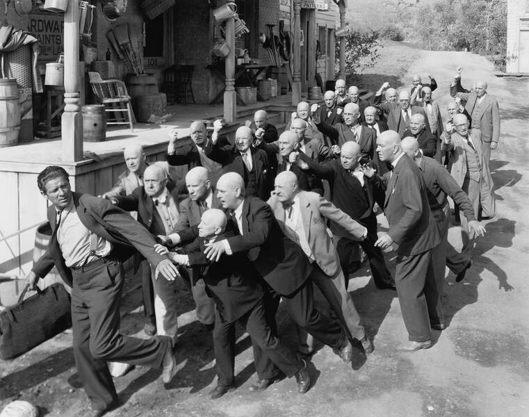 group of bald men running after a man with full set of hair